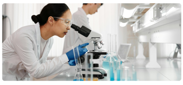 A biochemist looks through a microscope in a bright white lab environment